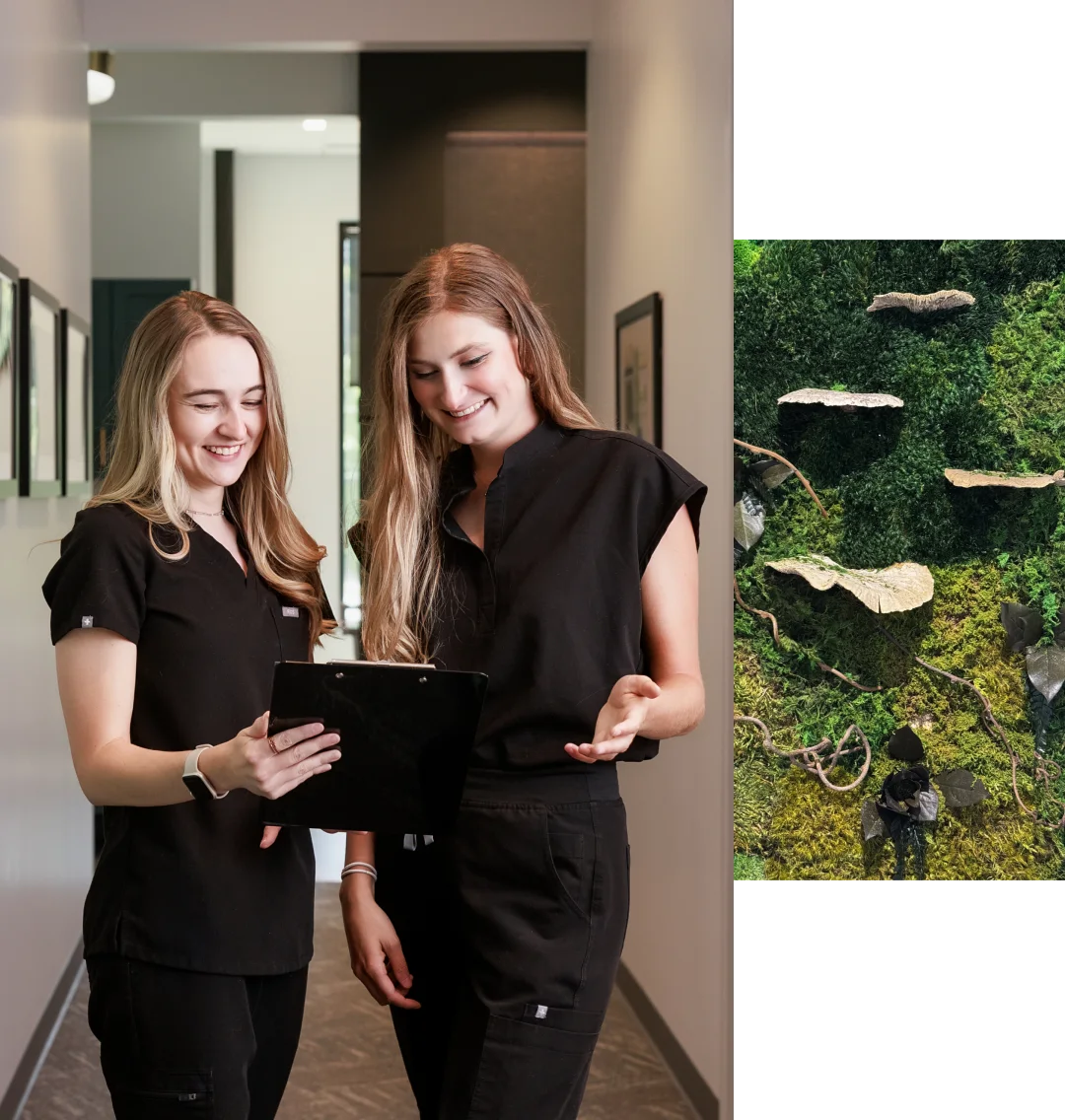 Two women in black uniforms smile and look at a tablet in a hallway; next to them is an image of rocks, branches, and greenery viewed from above.