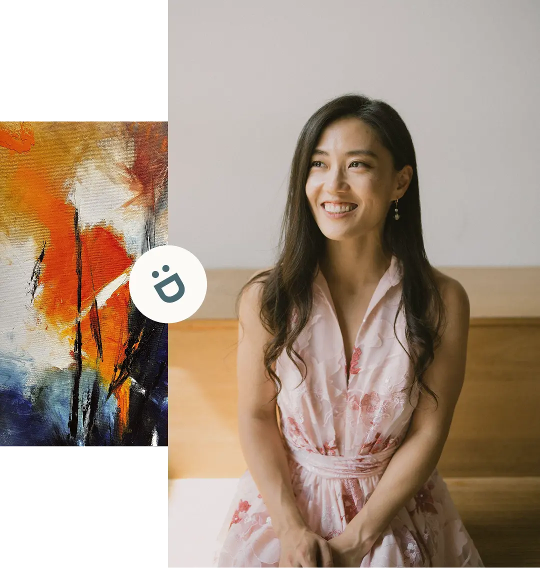 A woman with long dark hair smiles while sitting indoors. She wears a light pink blouse and earrings. An abstract painting with orange, blue, black, and white colors is partially visible at the bottom.